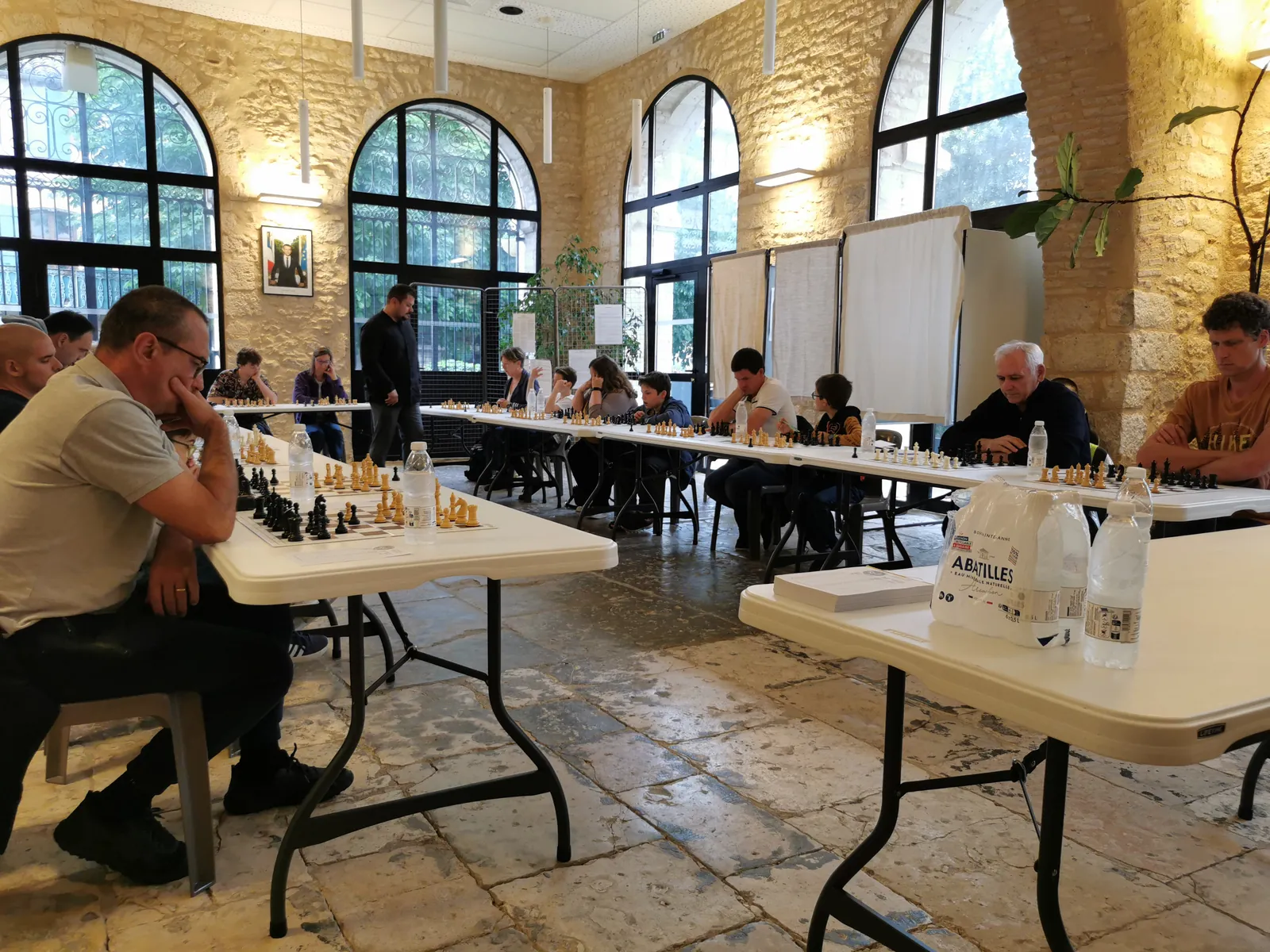 Joueuses et joueurs réunis autour des échiquiers dans la Salle de la Halle
